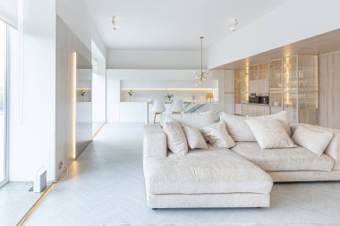 Beyaz ve bej renkli geniş tabandan tavana kadar pencereleri olan büyük bir stüdyonun modern iç tasarımı. Adayı ve dinlenme alanı olan beyaz mutfak.