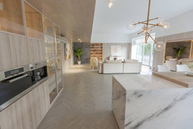 Beyaz ve bej renkli geniş tabandan tavana kadar pencereleri olan büyük bir stüdyonun modern iç tasarımı. Adayı ve dinlenme alanı olan beyaz mutfak.