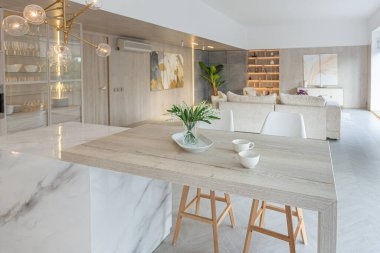 Beyaz ve bej renkli geniş tabandan tavana kadar pencereleri olan büyük bir stüdyonun modern iç tasarımı. Adayı ve dinlenme alanı olan beyaz mutfak.