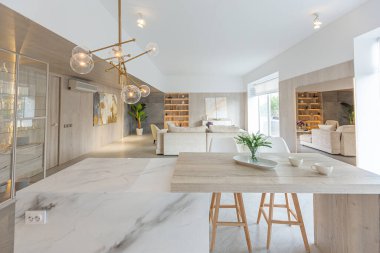 Beyaz ve bej renkli geniş tabandan tavana kadar pencereleri olan büyük bir stüdyonun modern iç tasarımı. Adayı ve dinlenme alanı olan beyaz mutfak.