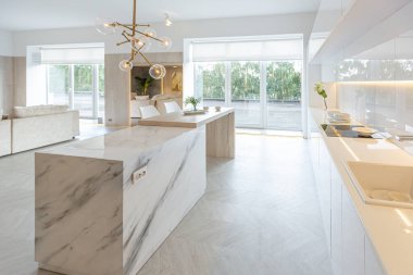 Modern moda kar beyazı mutfağının lüks iç tasarımı. Minimalist tarzda, ada ve iki bar taburesi. Yere kocaman pencereler ve bulaşıklar için cam askı.