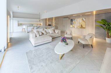 Beyaz ve bej renkli geniş tabandan tavana kadar pencereleri olan büyük bir stüdyonun modern iç tasarımı. Adayı ve dinlenme alanı olan beyaz mutfak.