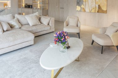 Stüdyo dairedeki oturma alanının sıcak ve yumuşak renklerde modern iç tasarımı. Dekoratif ışıklandırma ve yumuşak bej mobilyalar