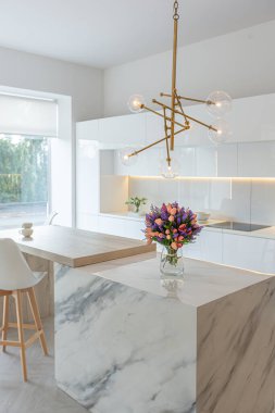 Modern moda kar beyazı mutfağının lüks iç tasarımı. Minimalist tarzda, ada ve iki bar taburesi. Yere kocaman pencereler ve bulaşıklar için cam askı.