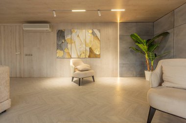 Stüdyo dairedeki oturma alanının sıcak ve yumuşak renklerde modern iç tasarımı. Dekoratif ışıklandırma ve yumuşak bej mobilyalar