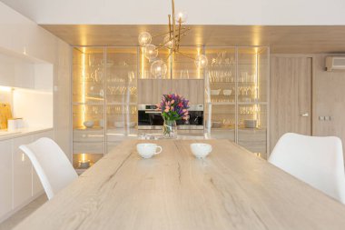 Modern moda kar beyazı mutfağının lüks iç tasarımı. Minimalist tarzda, ada ve iki bar taburesi. Yere kocaman pencereler ve bulaşıklar için cam askı.