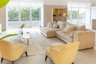 Stüdyo dairedeki oturma alanının sıcak ve yumuşak renklerde modern iç tasarımı. Dekoratif ışıklandırma ve yumuşak bej mobilyalar