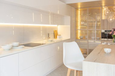 Modern moda kar beyazı mutfağının lüks iç tasarımı. Minimalist tarzda, ada ve iki bar taburesi. Yere kocaman pencereler ve bulaşıklar için cam askı.