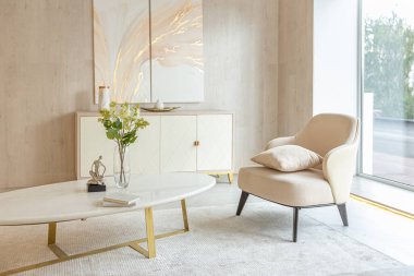 Stüdyo dairedeki oturma alanının sıcak ve yumuşak renklerde modern iç tasarımı. Dekoratif ışıklandırma ve yumuşak bej mobilyalar