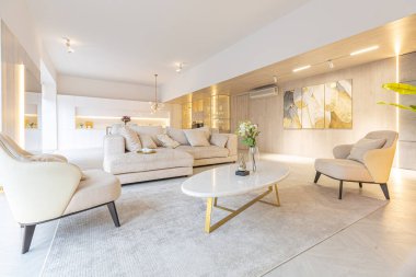 Beyaz ve bej renkli geniş tabandan tavana kadar pencereleri olan büyük bir stüdyonun modern iç tasarımı. Adayı ve dinlenme alanı olan beyaz mutfak.