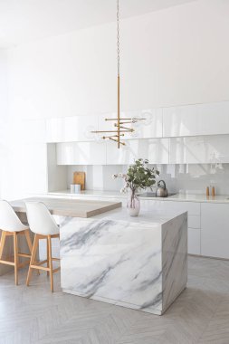 Modern moda kar beyazı mutfağının lüks iç tasarımı. Minimalist tarzda, ada ve iki bar taburesi. Yere kocaman pencereler ve bulaşıklar için cam askı.