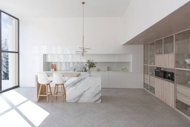 Modern moda kar beyazı mutfağının lüks iç tasarımı. Minimalist tarzda, ada ve iki bar taburesi. Yere kocaman pencereler ve bulaşıklar için cam askı.