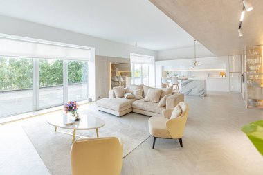 Beyaz ve bej renkli geniş tabandan tavana kadar pencereleri olan büyük bir stüdyonun modern iç tasarımı. Adayı ve dinlenme alanı olan beyaz mutfak.