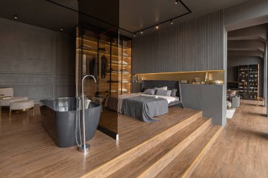 bedroom and freestanding bath behind a glass partition in a chic expensive interior of a luxury home with a dark modern design with wood trim and led light clipart