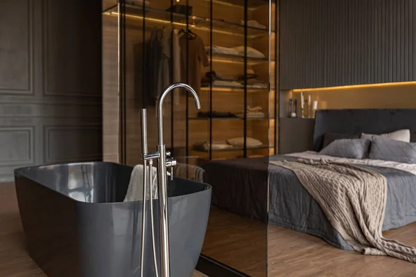 木製のトリムと光を導いたダークモダンデザインの高級住宅のシックな高価なインテリアのガラスのパーティションの後ろのベッドルームと自立風呂 — ストック写真