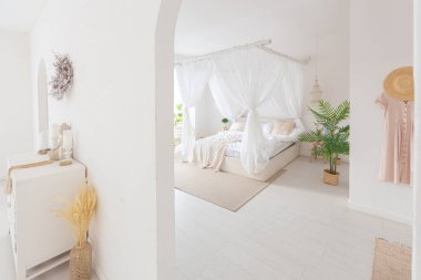 Beyaz duvarları, bambu mobilyaları olan, Bali tarzı parlak bir dairenin içi. Gece lambalı yatak odası, dengeli yatak ve geniş pencereli.