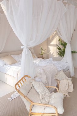 Beyaz duvarları, bambu mobilyaları olan, Bali tarzı parlak bir dairenin içi. Gece lambalı yatak odası, dengeli yatak ve geniş pencereli.