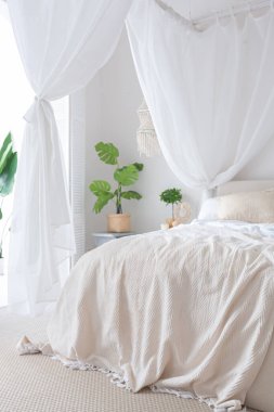 Beyaz duvarları, bambu mobilyaları olan, Bali tarzı parlak bir dairenin içi. Gece lambalı yatak odası, dengeli yatak ve geniş pencereli.