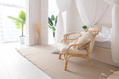 Beyaz duvarları, bambu mobilyaları olan, Bali tarzı parlak bir dairenin içi. Gece lambalı yatak odası, dengeli yatak ve geniş pencereli.