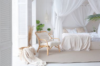 Beyaz duvarları, bambu mobilyaları olan, Bali tarzı parlak bir dairenin içi. Gece lambalı yatak odası, dengeli yatak ve geniş pencereli.