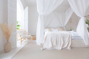 Beyaz duvarları, bambu mobilyaları olan, Bali tarzı parlak bir dairenin içi. Gece lambalı yatak odası, dengeli yatak ve geniş pencereli.