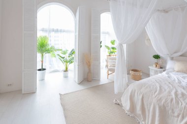 Beyaz duvarları, bambu mobilyaları olan, Bali tarzı parlak bir dairenin içi. Gece lambalı yatak odası, dengeli yatak ve geniş pencereli.