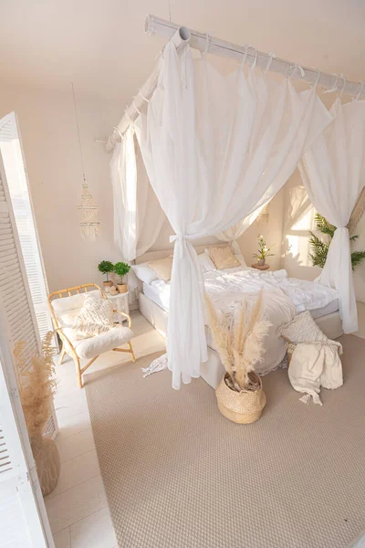 stock image Cozy interior of a bright Balinese-style apartment with white walls, bamboo furniture. bed room with night lights, bed with balanchin and large windows