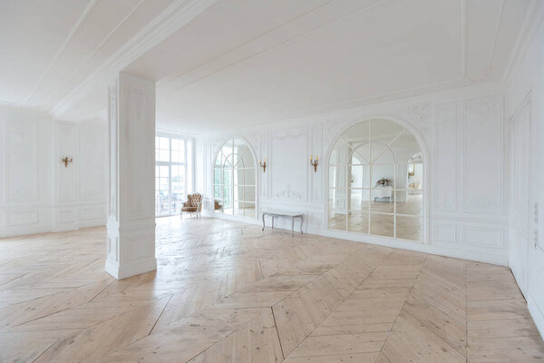 шикарный белый огромный просторный зал с минимальным количеством дорогой антикварной мебели. Интерьер в стиле барокко с орнаментом на стенах и паркетом на полу.