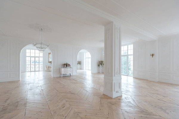 шикарный белый огромный просторный зал с минимальным количеством дорогой антикварной мебели. Интерьер в стиле барокко с орнаментом на стенах и паркетом на полу.