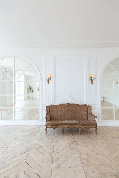 шикарный белый огромный просторный зал с минимальным количеством дорогой антикварной мебели. Интерьер в стиле барокко с орнаментом на стенах и паркетом на полу.