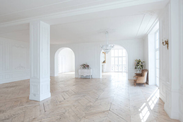 шикарный белый огромный просторный зал с минимальным количеством дорогой антикварной мебели. Интерьер в стиле барокко с орнаментом на стенах и паркетом на полу.