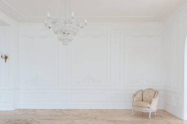 шикарный белый огромный просторный зал с минимальным количеством дорогой антикварной мебели. Интерьер в стиле барокко с орнаментом на стенах и паркетом на полу.