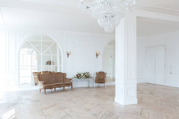 шикарный белый огромный просторный зал с минимальным количеством дорогой антикварной мебели. Интерьер в стиле барокко с орнаментом на стенах и паркетом на полу.