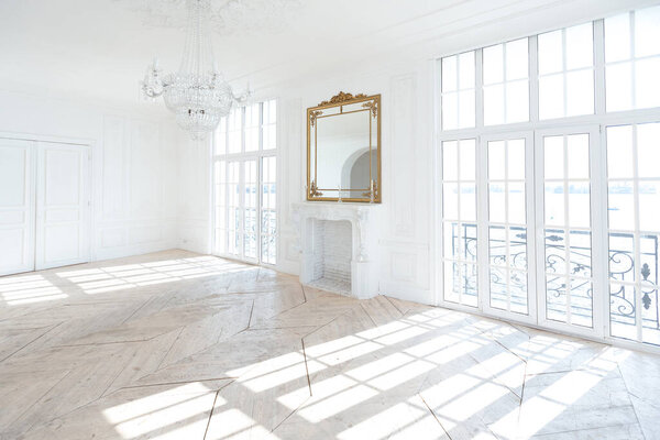 шикарный белый огромный просторный зал с минимальным количеством дорогой антикварной мебели. Интерьер в стиле барокко с орнаментом на стенах и паркетом на полу.