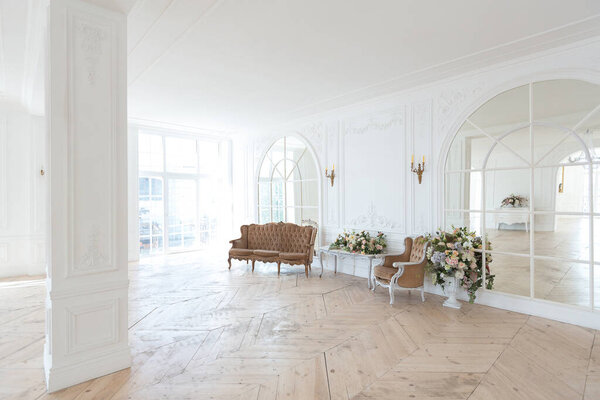 шикарный белый огромный просторный зал с минимальным количеством дорогой антикварной мебели. Интерьер в стиле барокко с орнаментом на стенах и паркетом на полу.