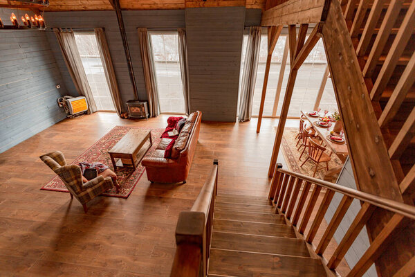 уютный весь деревянный интерьер загородного дома в деревянном дизайне. просторная гостиная с кухней и большими окнами. спальня на втором этаже.