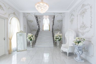 Barok tarzında lüks kraliyet iç mimarisi. Pahalı eski tarz mobilyaları olan aydınlık ve beyaz bir salon. İkinci kata çıkan şık geniş mermer merdiven.