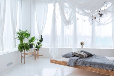 Geniş, ferah, şık, açık bir Bali tarzı dairesi asılı yatağı ve panoramik pencereleri var. Beyaz zemin ve duvarlar, basit ahşap mobilyalar..