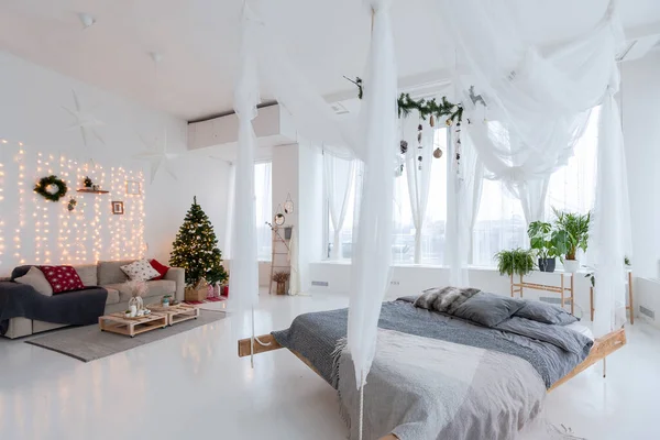 stock image large very bright spacious stylish open plan Bali style apartment with hanging bed and panoramic windows. white floor and walls, simple wooden furniture. decorated with a christmas tree