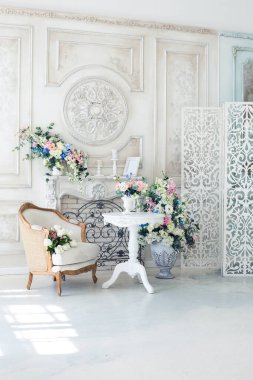 Parlak, beyaz ve mavi renkli, vazolarında çiçekler olan bir oturma odası. Duvarlar barok süslemelerle süslenmiş.