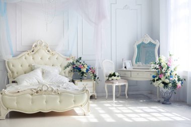 Parlak, beyaz ve mavi renkli, vazolarında çiçekler olan bir oturma odası. Duvarlar barok süslemelerle süslenmiş.