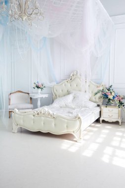 Parlak, beyaz ve mavi renkli, vazolarında çiçekler olan bir oturma odası. Duvarlar barok süslemelerle süslenmiş.