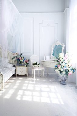 Parlak, beyaz ve mavi renkli, vazolarında çiçekler olan bir oturma odası. Duvarlar barok süslemelerle süslenmiş.