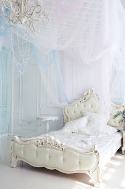 Parlak, beyaz ve mavi renkli, vazolarında çiçekler olan bir oturma odası. Duvarlar barok süslemelerle süslenmiş.