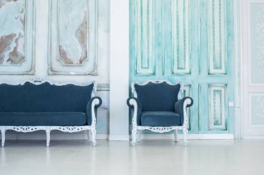 Parlak, beyaz ve mavi renkli, vazolarında çiçekler olan bir oturma odası. Duvarlar barok süslemelerle süslenmiş.