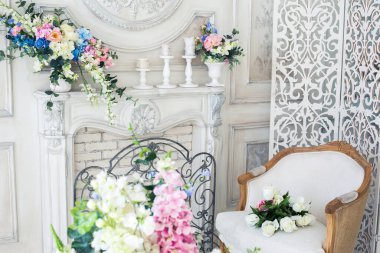 Parlak, beyaz ve mavi renkli, vazolarında çiçekler olan bir oturma odası. Duvarlar barok süslemelerle süslenmiş.