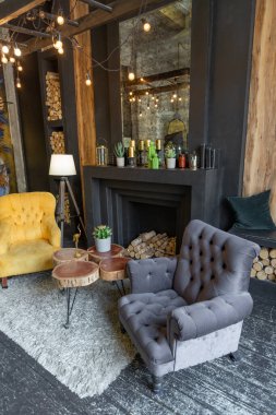 Oturma odasının içi tahtadan kütüklerle süslenmiş. sarı ve gri yumuşak koltuklar, büyük kavisli pencere ve şömine