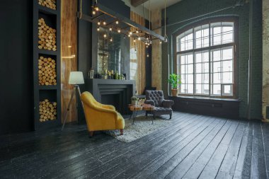 Oturma odasının içi tahtadan kütüklerle süslenmiş. sarı ve gri yumuşak koltuklar, büyük kavisli pencere ve şömine
