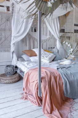 Bali tarzı yatak odasının içi. Dekorasyon için bir sürü tekstil ve yumuşak pastel renklerde hasır eşyalar içeren tenteli yatak.