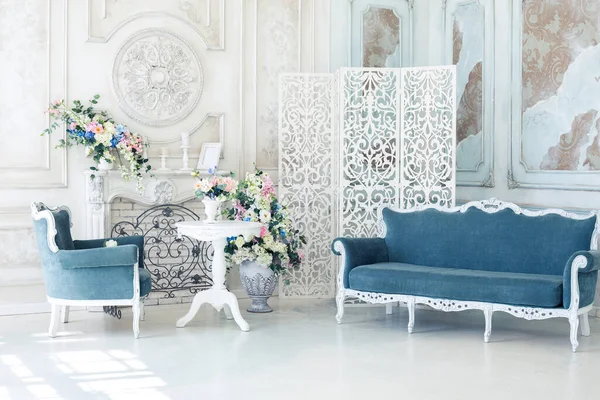 Bright luxury white and blue colored interior living room with flowers in vases. the walls are decorated with baroque ornaments